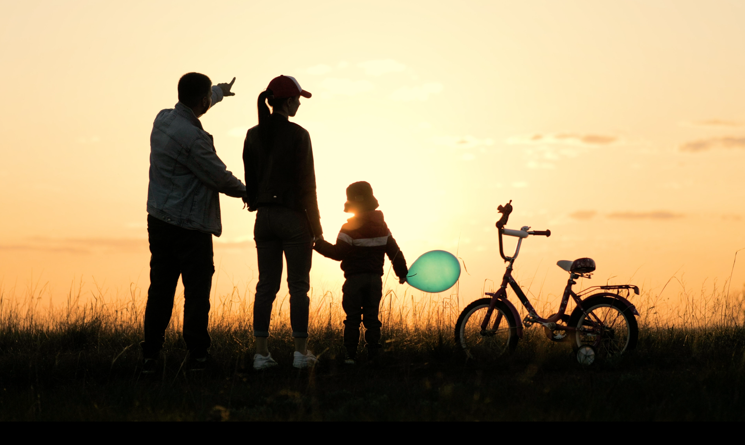 Screenshot of stock footage item on. Scene shows a family of two adults and a young child silhouetted against a sunset. A child's bike is near them 