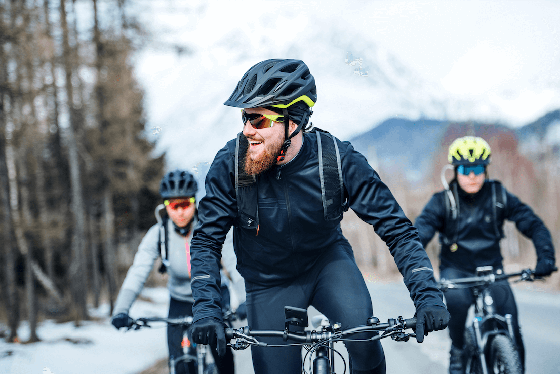Three people dressed in black riding bikes through mountains in the snow.