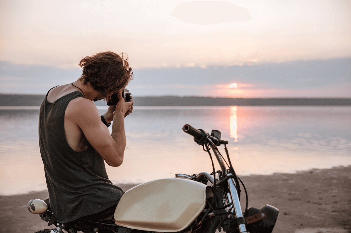 A photo from the 'summer vibes' collection, curated by our photo & video review teams. This photo depicts a man taking a photo of a sunset while sitting on a motorbike.