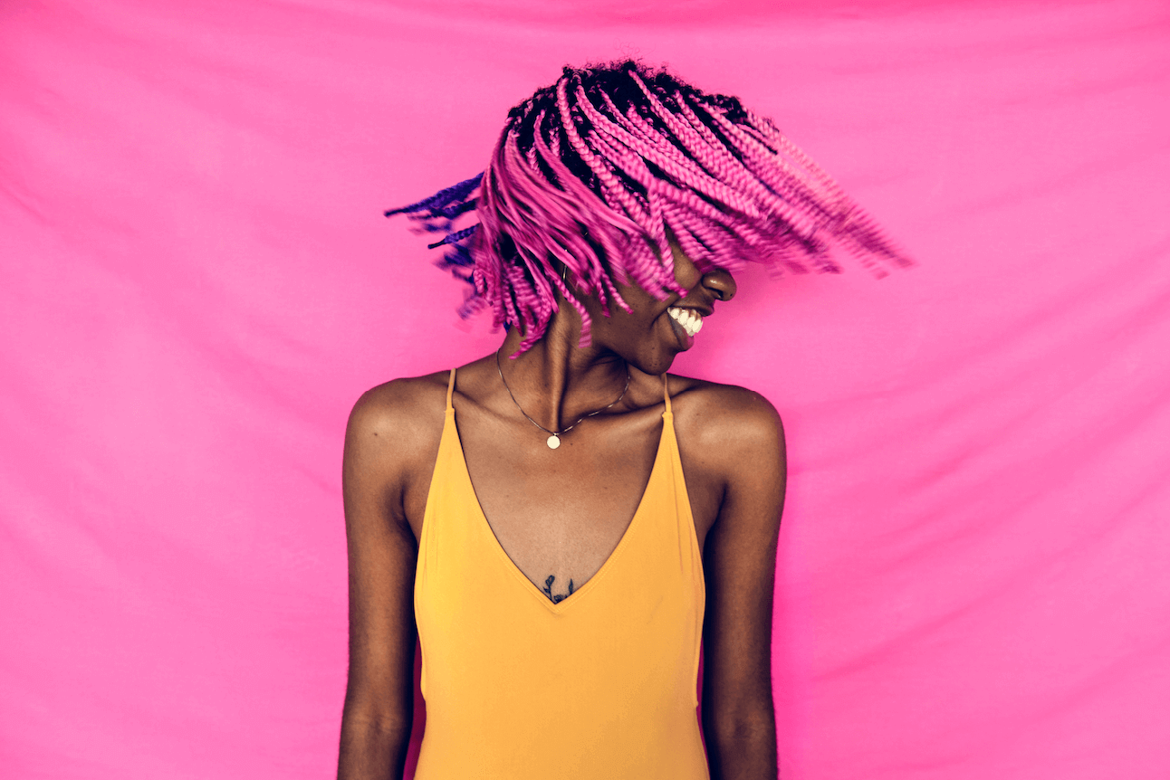 A photo from the 'summer vibes' collection, curated by our photo & video review teams. This photo depicts a Black woman with pink hair on a pink background.